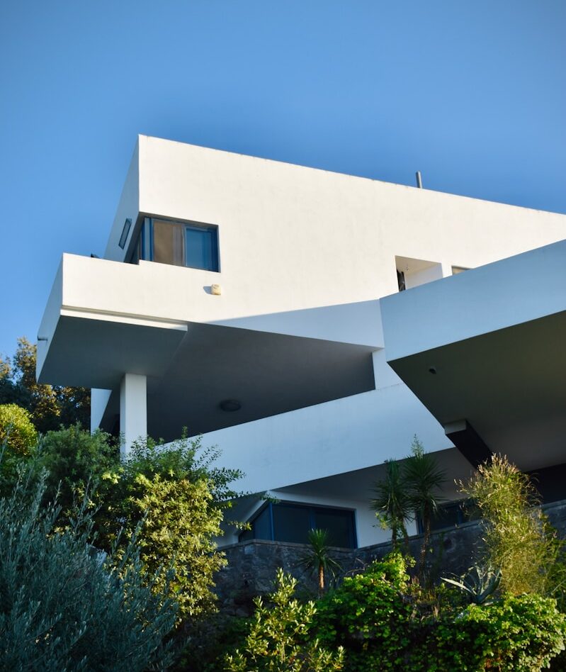 Photo by Arno Senoner white concrete building near green trees under blue sky during daytime